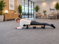 Woman using Movelio Bed Roller Professional for thigh massage in a bright workplace lounge.